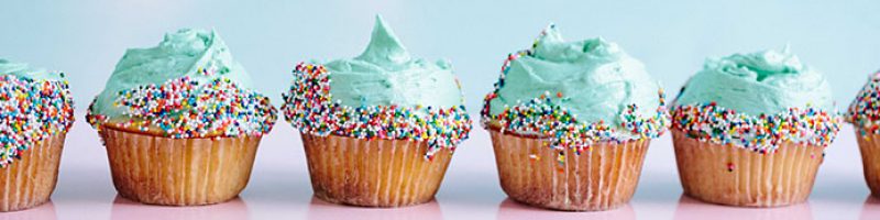 a row of blue cupcakes decorated with colorful sprinkles