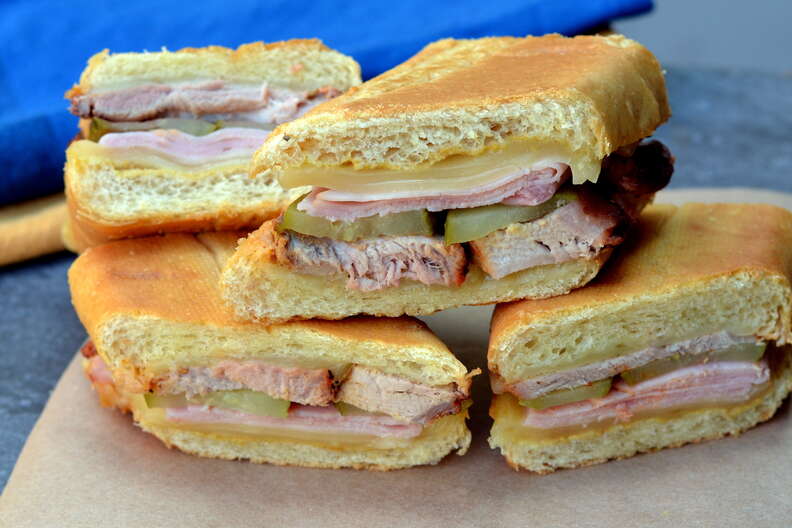 a pressed sandwich with layers of pork, pickles, ham, and cheese