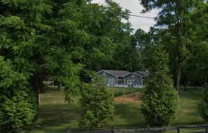 Gray and white barn in a green pasture surrounded by trees