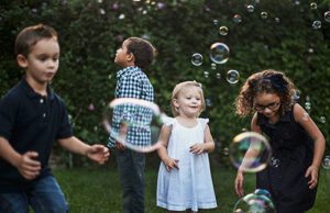 Kids chasing bubbles in a green grassy area.