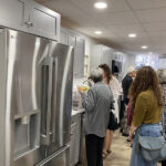 A group of people in an updated kitchen with gray cabinets and a stainless steel refrigerator