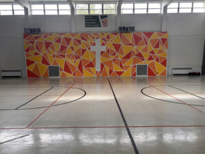 Orange and yellow abstract shapes form a large backdrop in the gymnasium with a white cross in the middle